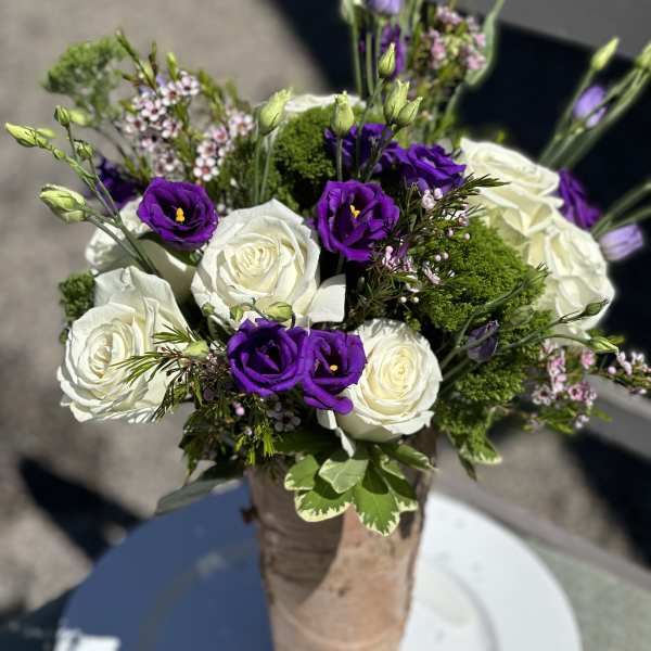 Bouquet of white roses and purple lisianthus in a wrapped vase
