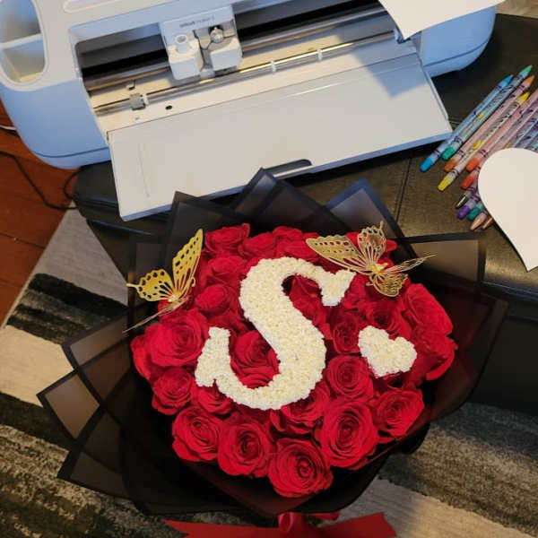 Round bouquet of red roses with a white floral letter S and gold butterflies in black wrap.