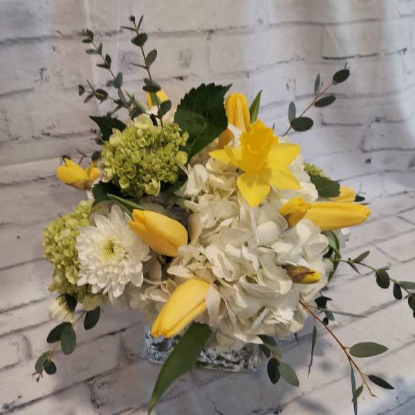 Yellow tulips and white flowers in a clear glass vase