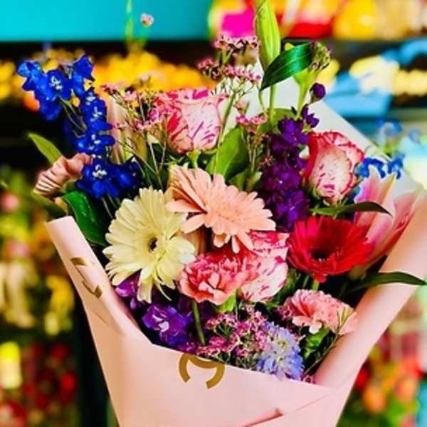 Mixed bouquet with gerbera daisies, carnations, and purple flowers in pink wrap