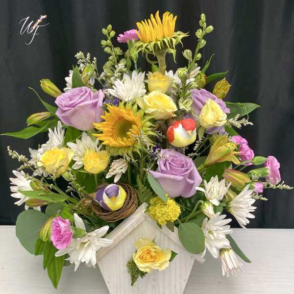 Mixed bouquet in a white wooden vase with sunflowers, roses, and daisies