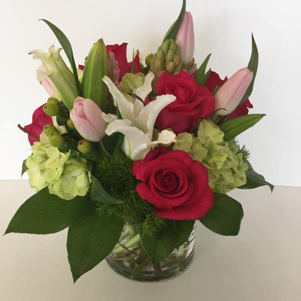 Bouquet of red roses, pink tulips, white lilies, and green hydrangeas in a glass vase