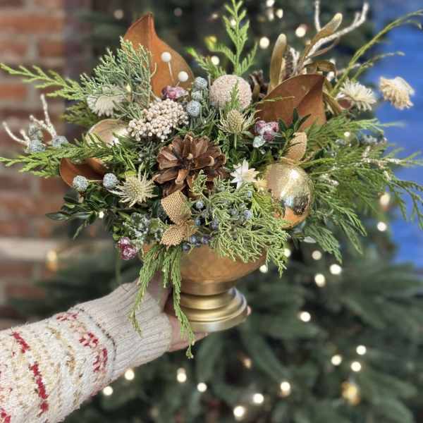 Holiday arrangement with pinecones, greenery, and gold ornaments in a gold vase