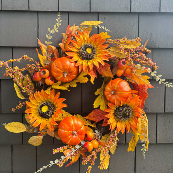 Autumn wreath with sunflowers, pumpkins, and berries on a dark wall