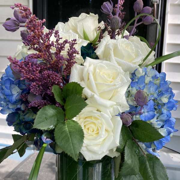 White roses and blue hydrangeas in a glass vase with purple accents