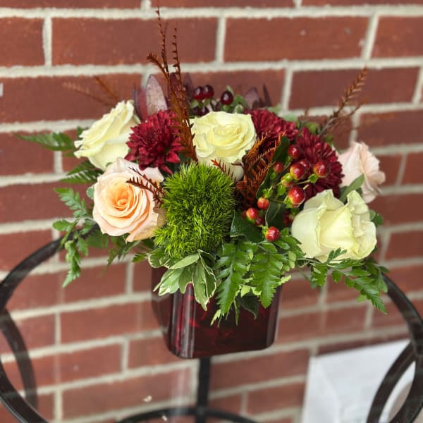 Mixed rose arrangement in a dark red vase with greenery