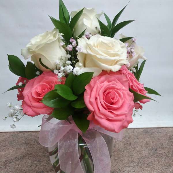 Pink and white roses arranged in a glass vase with a pink ribbon