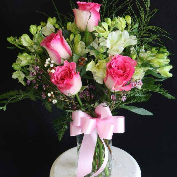 Pink roses and white alstroemeria in a glass vase with a pink ribbon