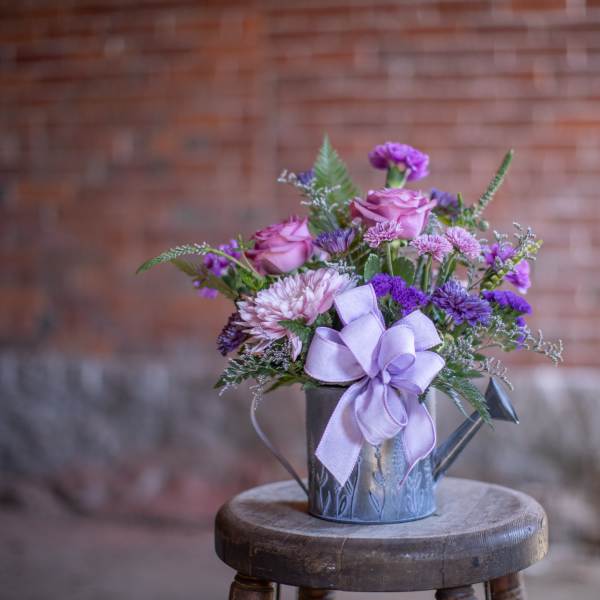 Purple and pink flower arrangement in a small metal watering can with a lavender bow