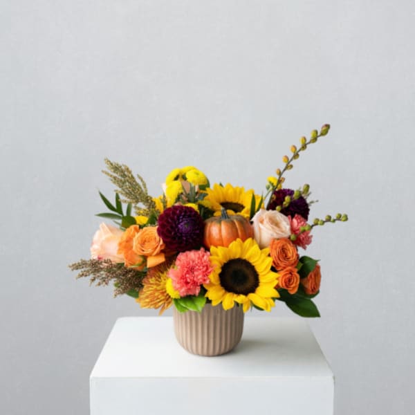 Mixed bouquet with sunflowers, roses, and a small pumpkin in a ribbed vase