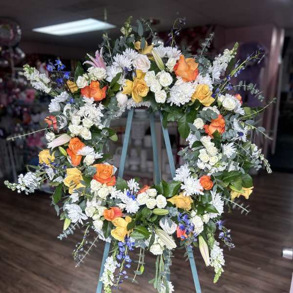 Large floral wreath on a stand with orange, yellow, white, and blue flowers