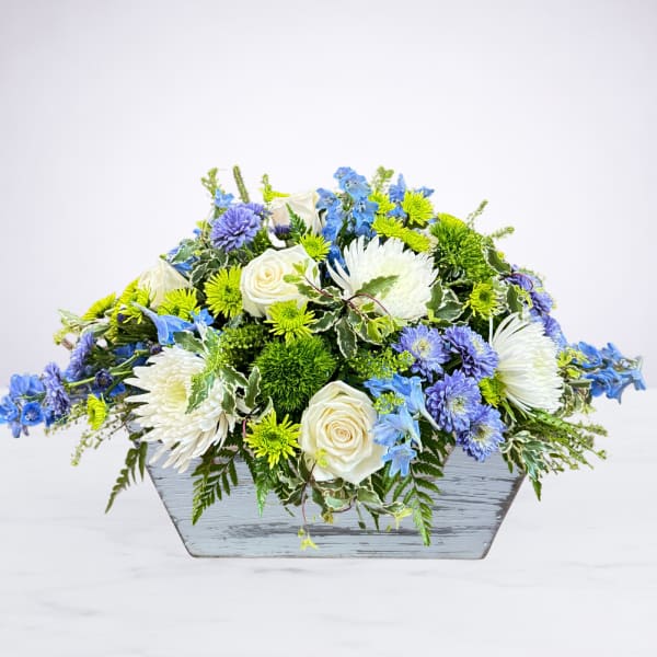 Blue, white, and green floral arrangement in a gray wooden container