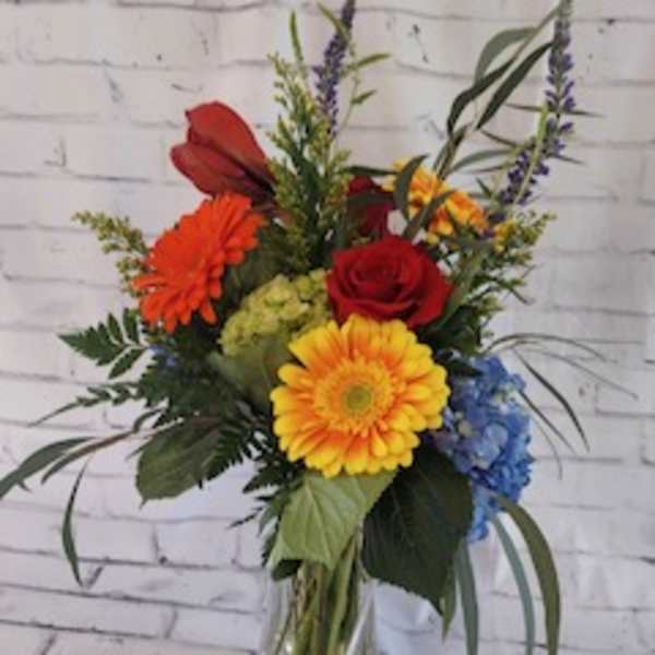 Mixed bouquet in a clear glass vase with red, yellow, orange, and blue flowers