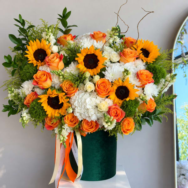 Large bouquet of orange roses, sunflowers, and white blooms in a green vase