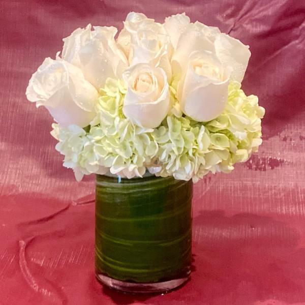 White roses and pale hydrangeas in a green glass vase