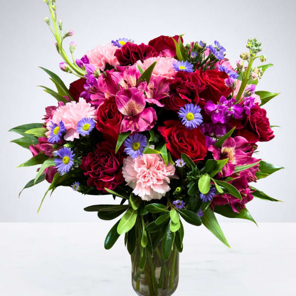 Mixed bouquet of red, pink, and purple flowers in a glass vase