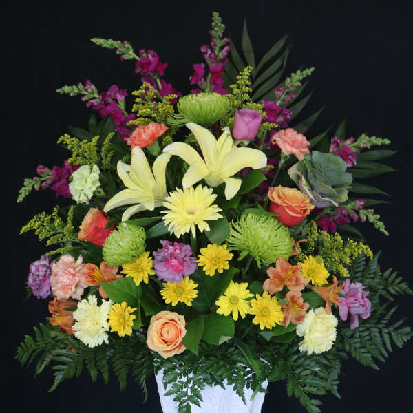 Mixed bouquet in a white pedestal vase with yellow lilies and roses