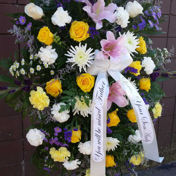 Standing sympathy spray with yellow and white roses, lilies, and purple flowers