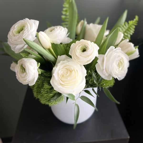 White ranunculus and roses arranged in a white vase