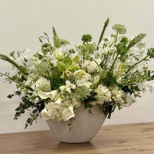 White and green flower arrangement in a textured white bowl on a wooden surface