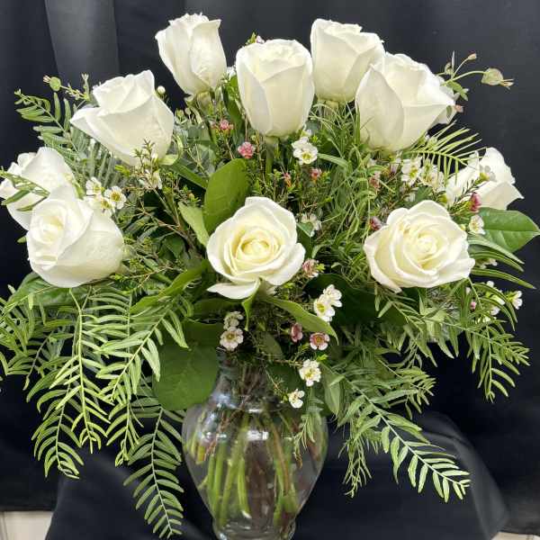 White roses arranged in a clear glass vase with mixed greenery