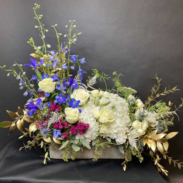 Mixed floral arrangement with white roses, blue flowers, and gold foliage in a low container