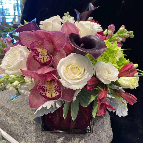 Bouquet of white roses, pink orchids, and dark calla lilies in a vase