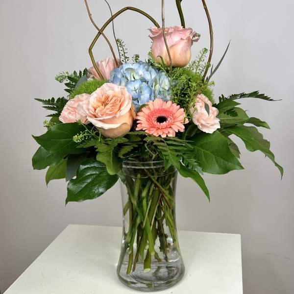 Pink roses and a blue hydrangea in a clear glass vase
