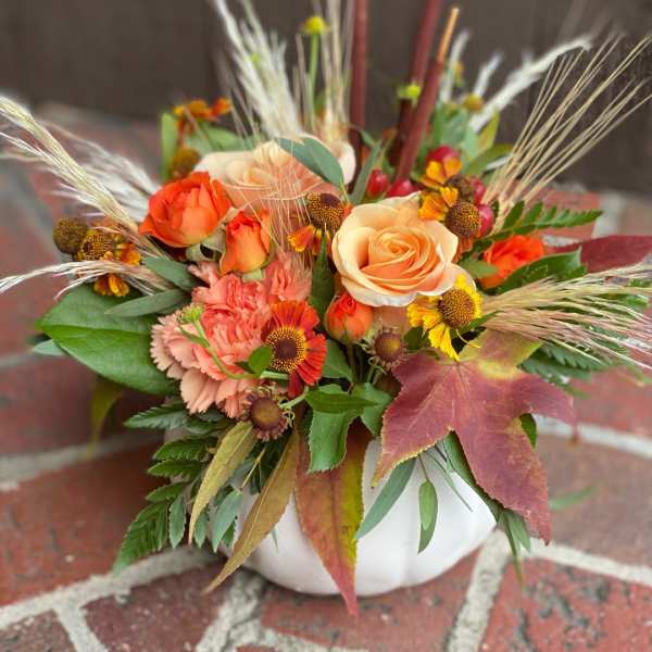 Orange and peach roses in a white vase with autumn flowers