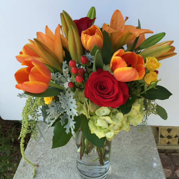 Bouquet of orange lilies, red roses, and yellow blooms in a glass vase