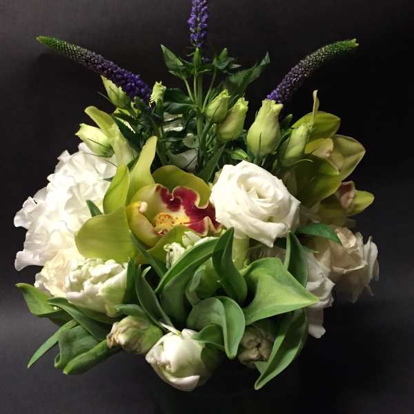White and green floral arrangement with purple spikes in a black vase
