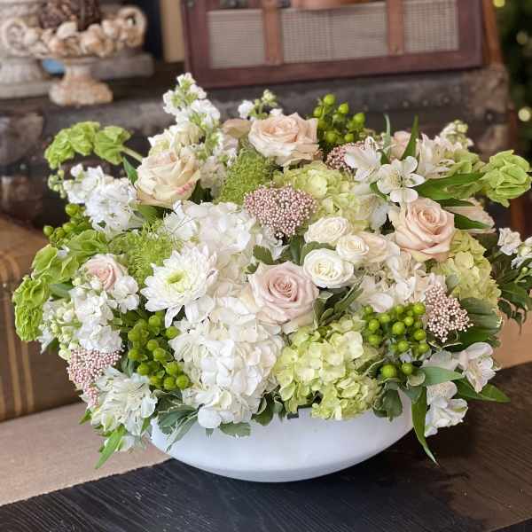 Low floral arrangement of pale roses, hydrangeas, and white blooms in a white bowl