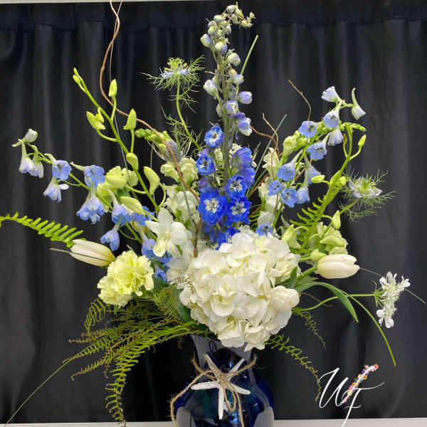 Tall blue and white floral arrangement in a dark vase