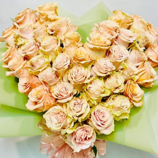 Heart-shaped bouquet of pale peach roses wrapped in green paper