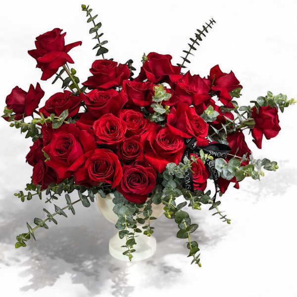 Red roses arranged in a white vase with trailing greenery