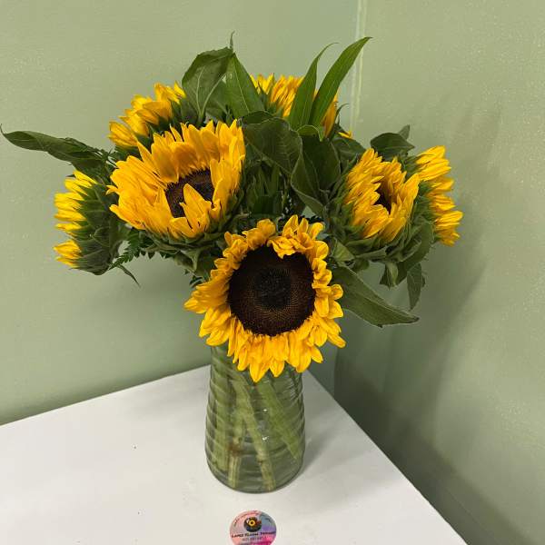 Vase arrangement of yellow sunflowers with dark centers in a clear glass vase on a white table