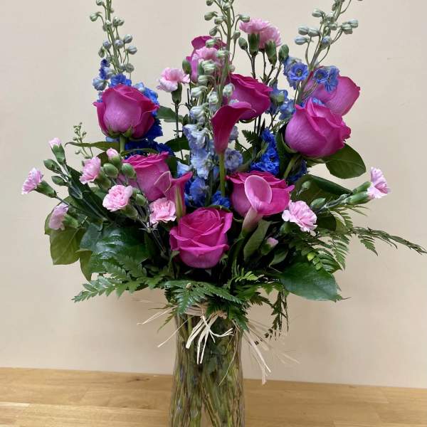 Bouquet of pink roses, blue flowers, and calla lilies in a glass vase