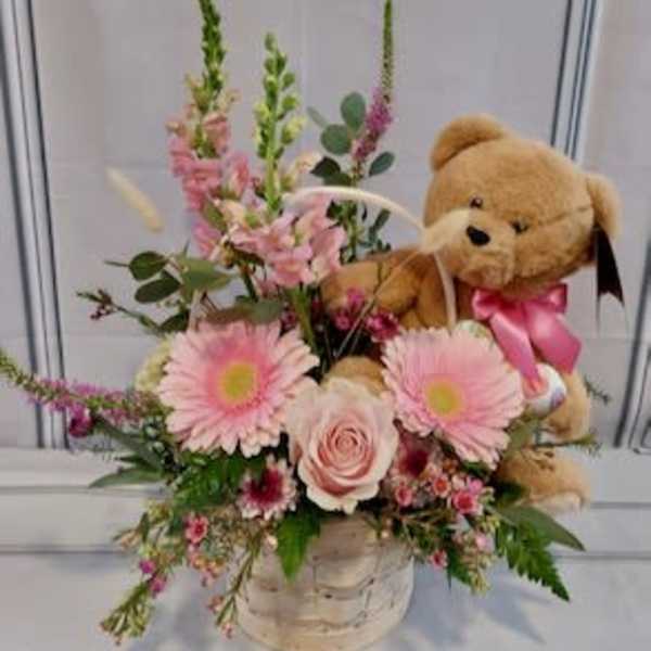 Pink flower arrangement with a teddy bear in a basket