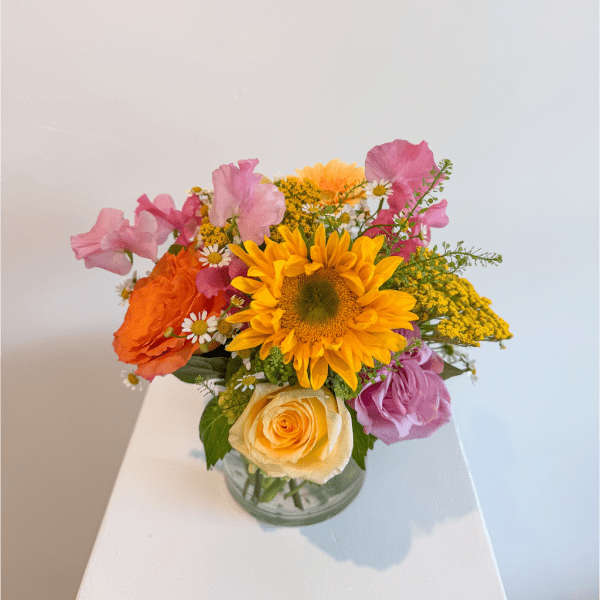 Colorful bouquet in a clear glass vase with a sunflower and roses