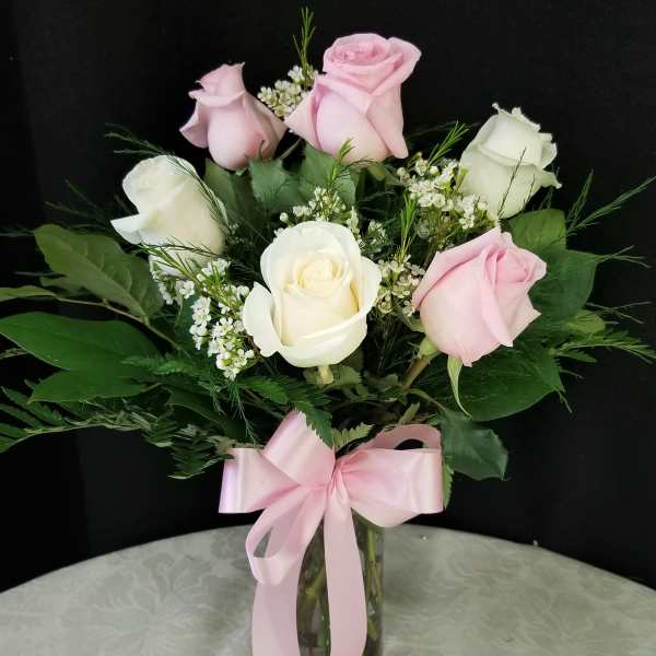 Pink and white roses in a glass vase with a pink ribbon