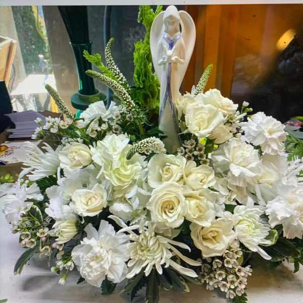 White floral arrangement with roses and carnations around a figurine centerpiece