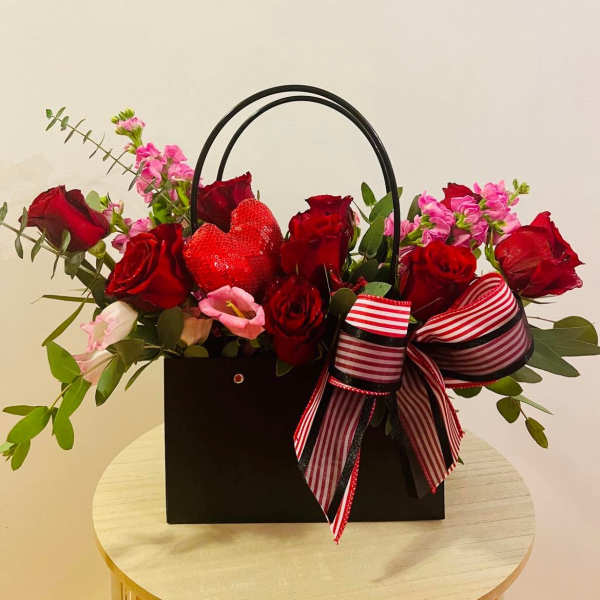 Black gift bag with red roses and pink flowers, topped with a strawberry heart