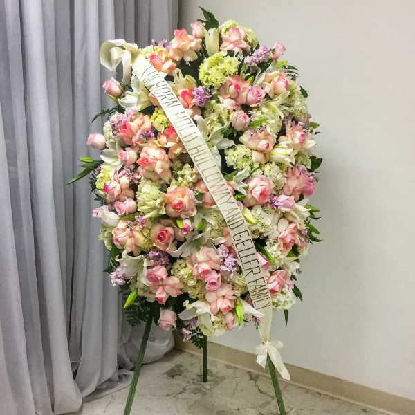 Standing funeral wreath of pink and white flowers with a condolence ribbon