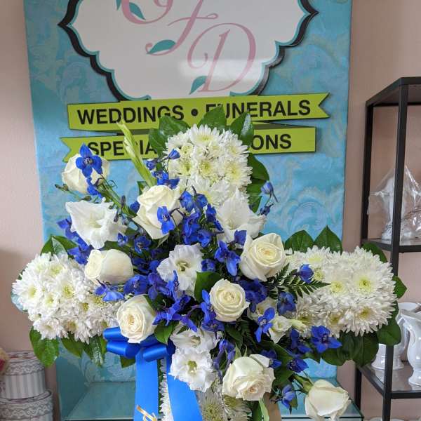 White and blue funeral standing spray on an easel with ribbon streamers