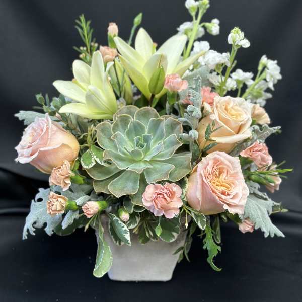 Peach roses and lilies arranged with a succulent in a square vase