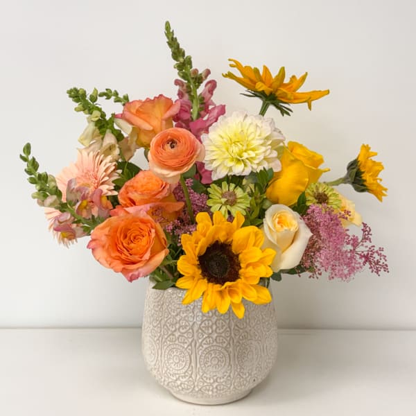 Mixed bouquet of orange, yellow, pink, and white flowers in a patterned vase