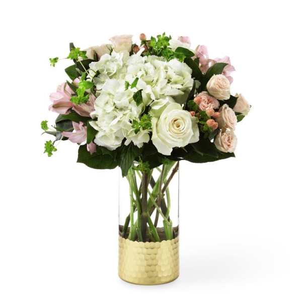White and blush flowers arranged in a tall glass vase with a gold base