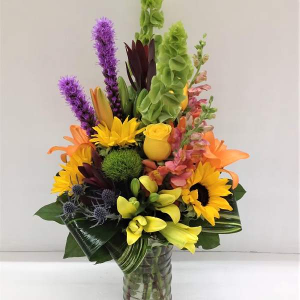 Colorful bouquet with sunflowers, lilies, and purple spikes in a glass vase