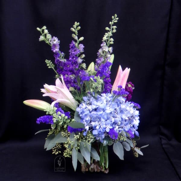 Purple and blue floral arrangement with lilies and hydrangeas in a glass vase