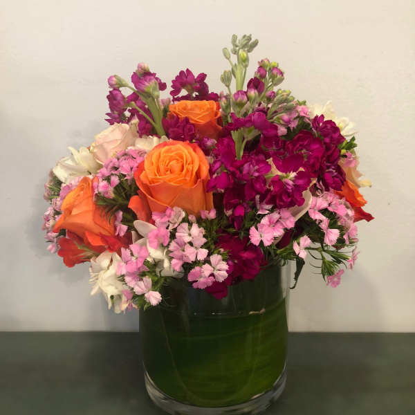 Mixed bouquet of orange roses, pink flowers, and white blooms in a glass vase